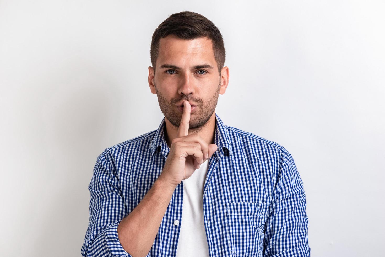 Hombre en ropa casual haciendo un gesto de silencio con el dedo en el estudio.- imagen foto