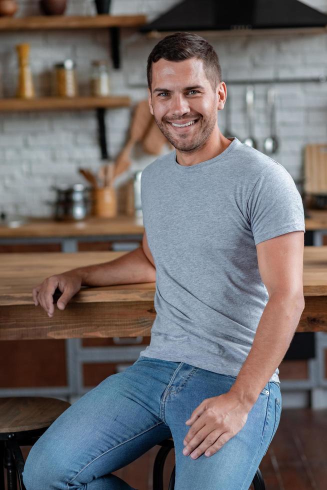 Hombre guapo se sienta en la silla apoyado en la mesa, sonriendo mirando a la cámara.- imagen foto