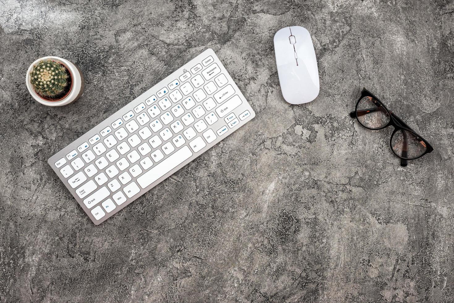 Fondo de yeso de vista superior con teclado, gafas, ratón y un cactus. - copyspace foto