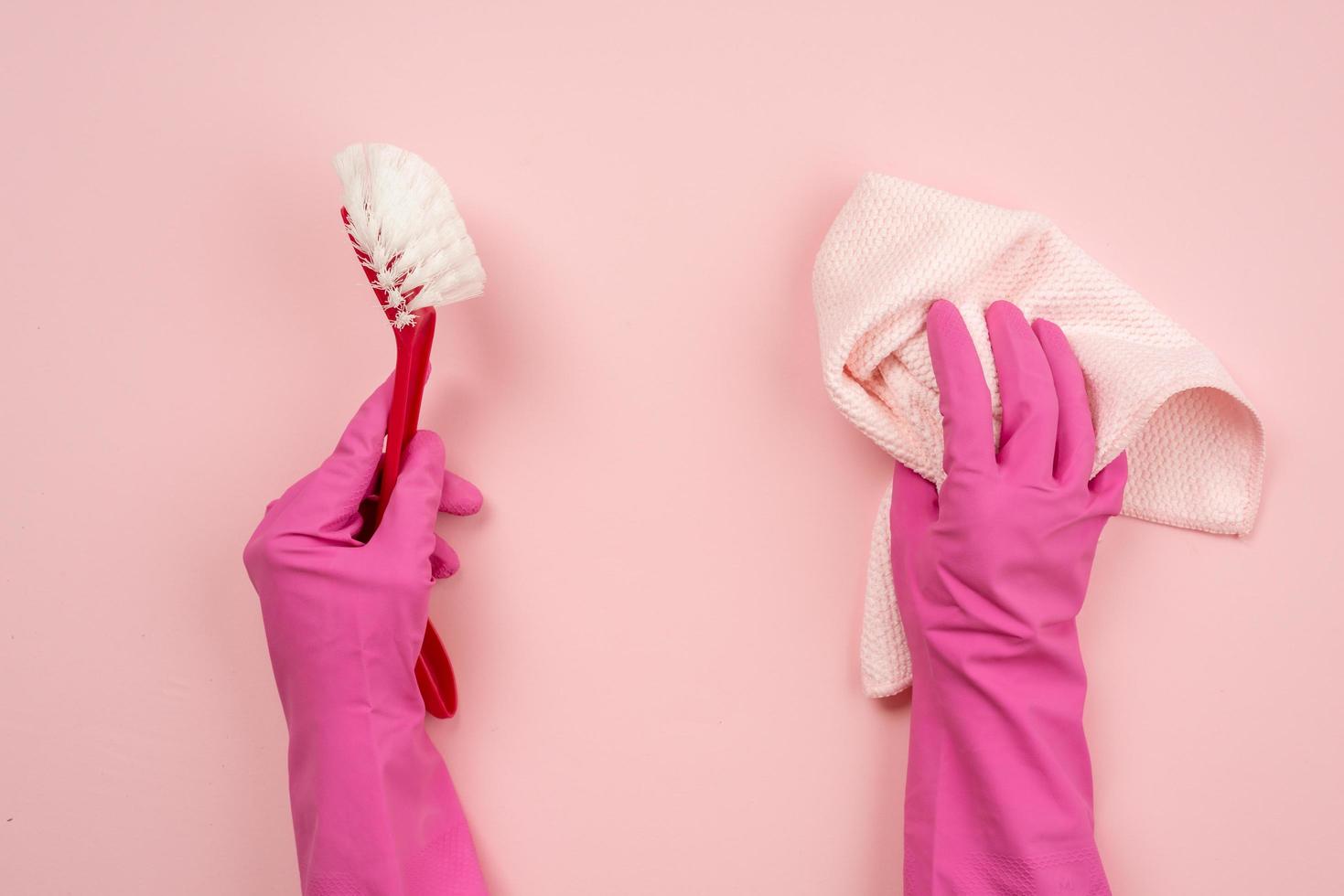Closeup hands wearing in latex gloves holding a rag and household brush. Top view on pink background photo