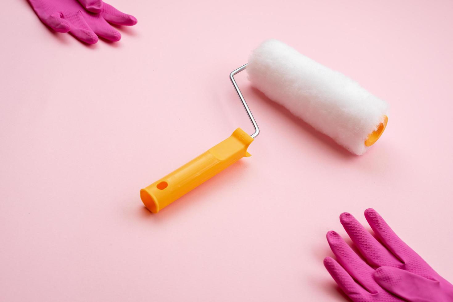 paint roller  and latex gloves lying on diagonal on pink background photo