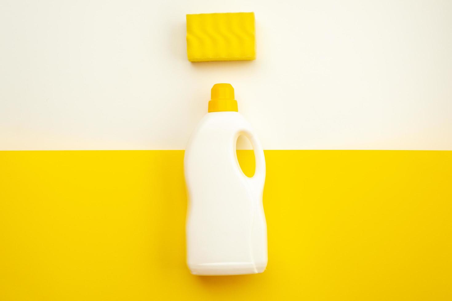 Botella de detergente con tapón amarillo y esponja sobre un fondo blanco-amarillo foto