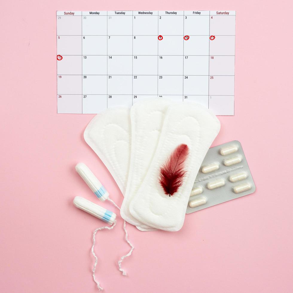 Menstrual calendar, woman pads, tampons and pills for period pain lying on red background. - Image photo