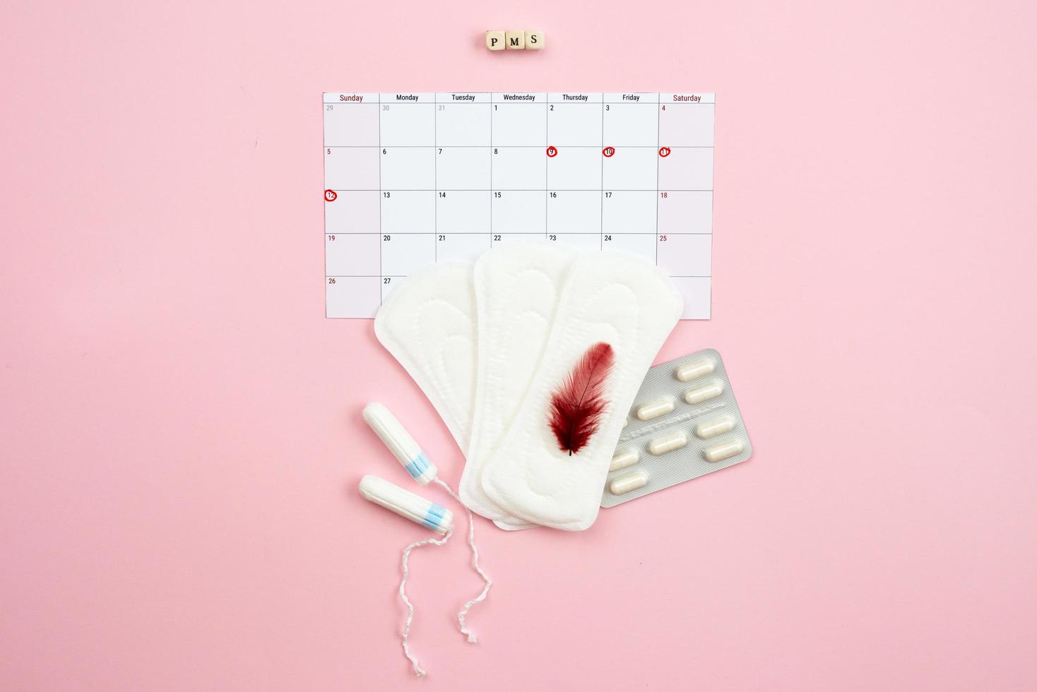 Tampon, feminine, sanitary pads for critical days, feminine calendar, pain pills during menstruation and a red feather on a pink background. Care of hygiene during menstruation. photo