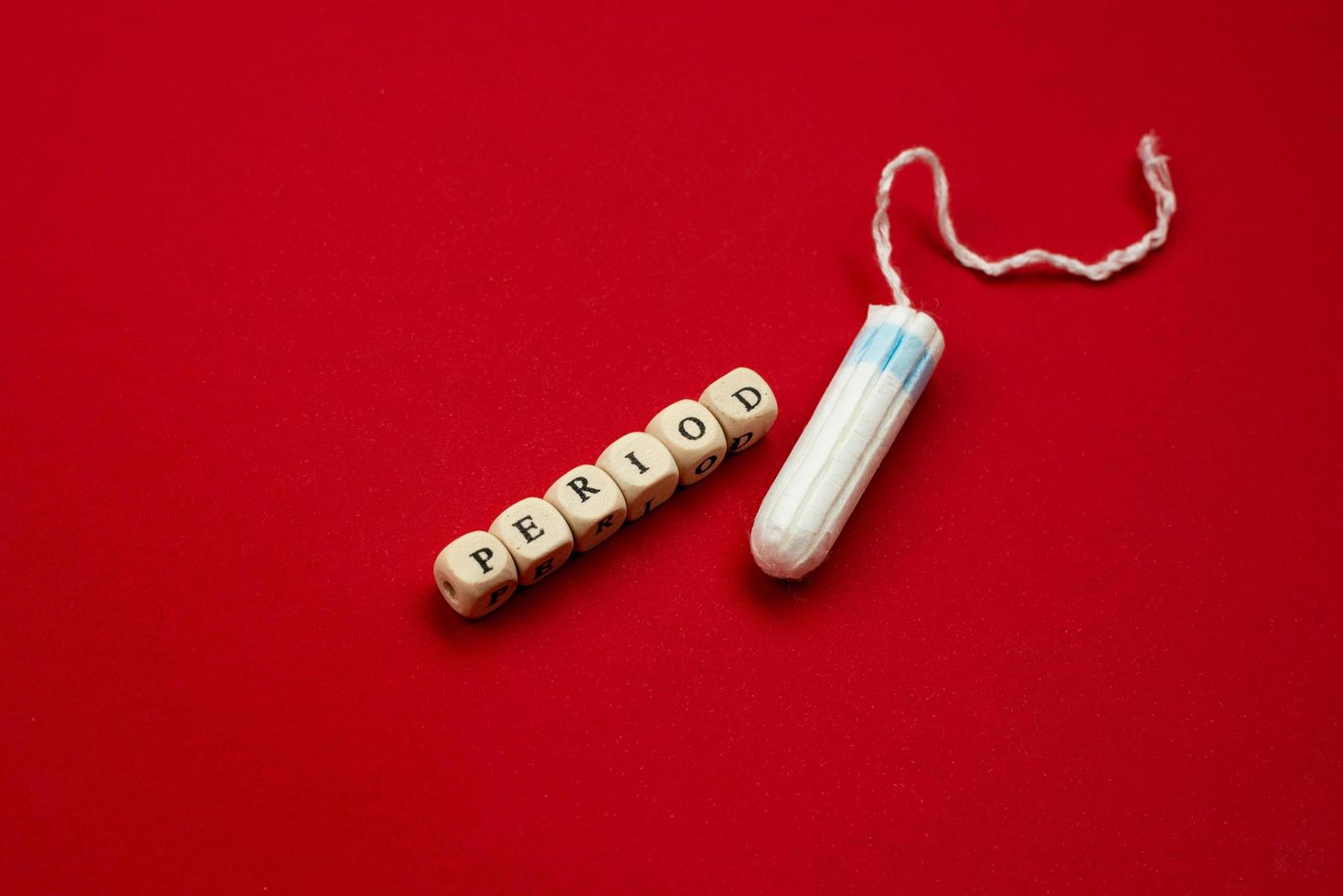 Tampon lying isolated on red background with text period. Concept women sanitary protect photo