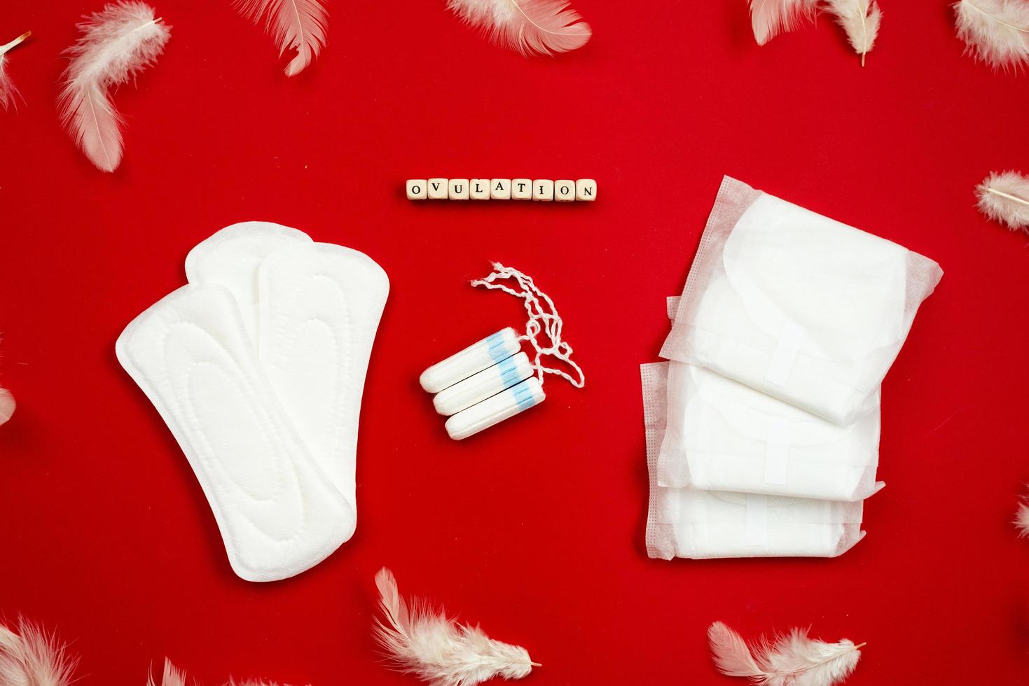 Top view with white feathers, woman pads and tampons lying on red background. - Image photo