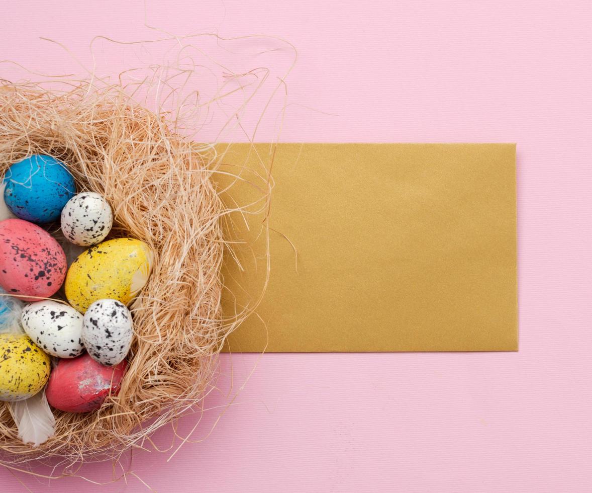 huevos de pascua en nido y tarjeta de saludos sobre fondo rosa foto