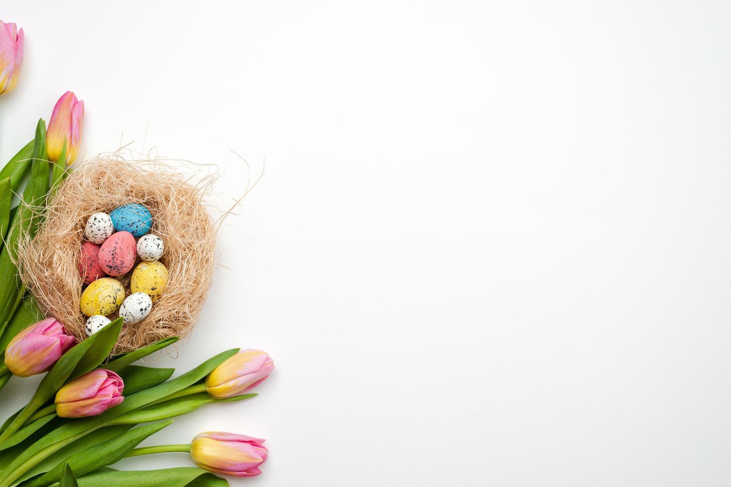 Fondo de Pascua, huevos multicolores y ramo de tulipanes se encuentran sobre una mesa blanca. - copia espacio foto