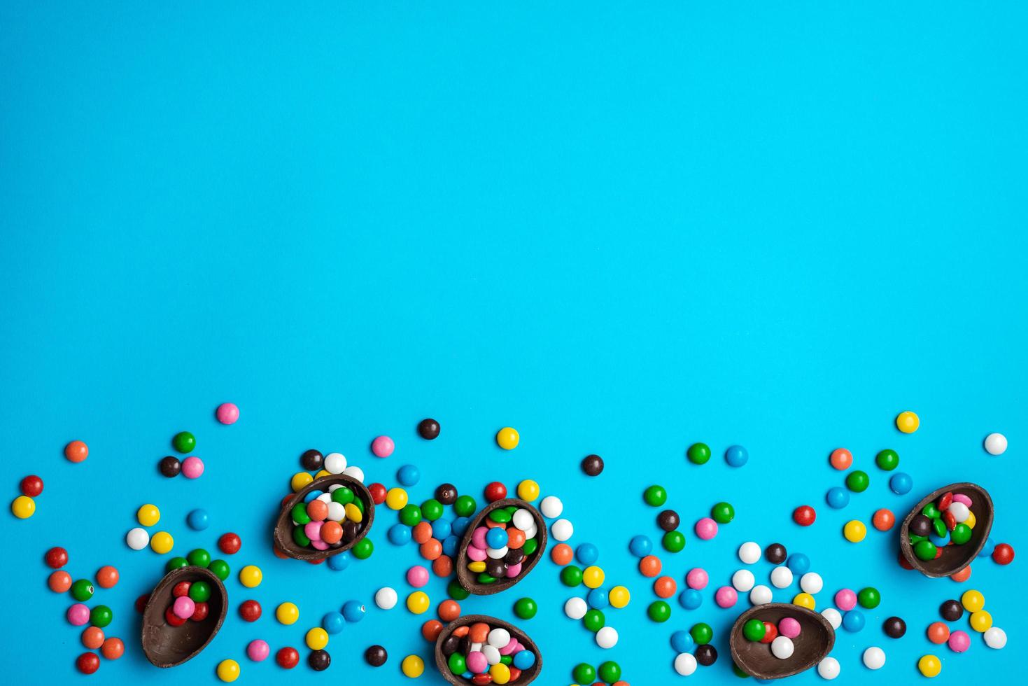 huevo de pascua de chocolate con colorida explosión de caramelos y dulces sobre un fondo azul. endecha plana. vista superior foto