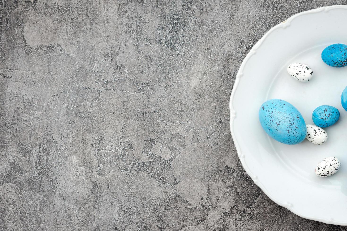 Huevos de Pascua azules y blancos en un plato sobre un fondo de yeso gris. - copyspace foto