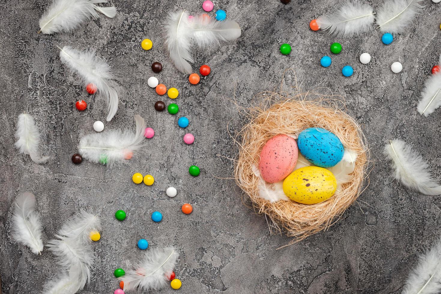 Easter background. Multi-colored eggs in a nest. Candy and feathers scattered on a grey plaster background photo