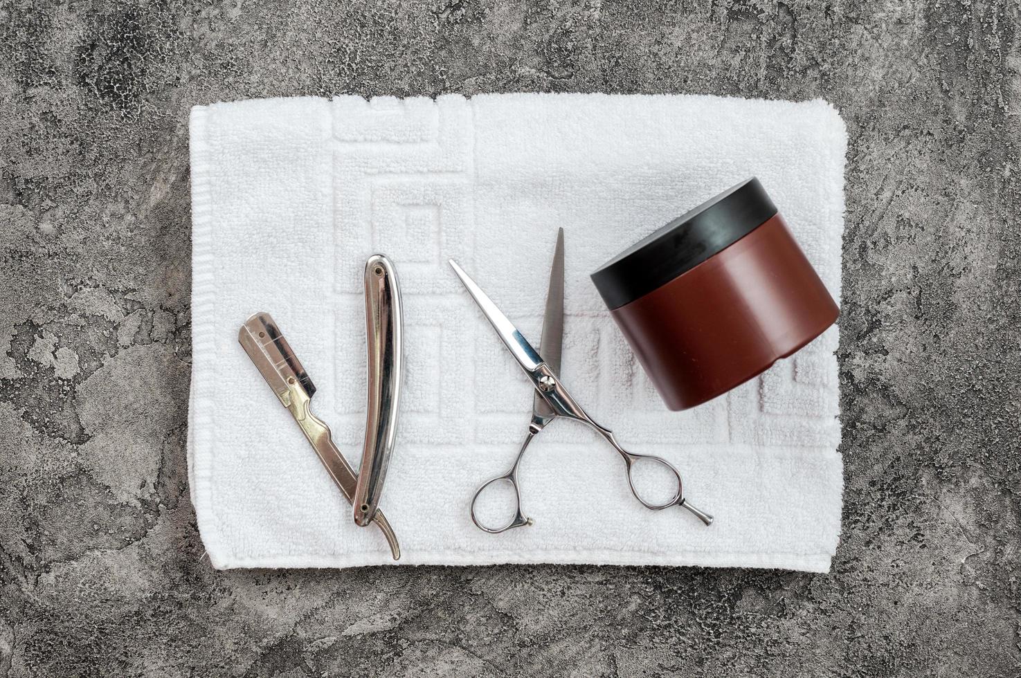 On a gray, plaster background unfolded towel, it has a razor, scissors and styling gel. Concept of male shaving, haircut. photo