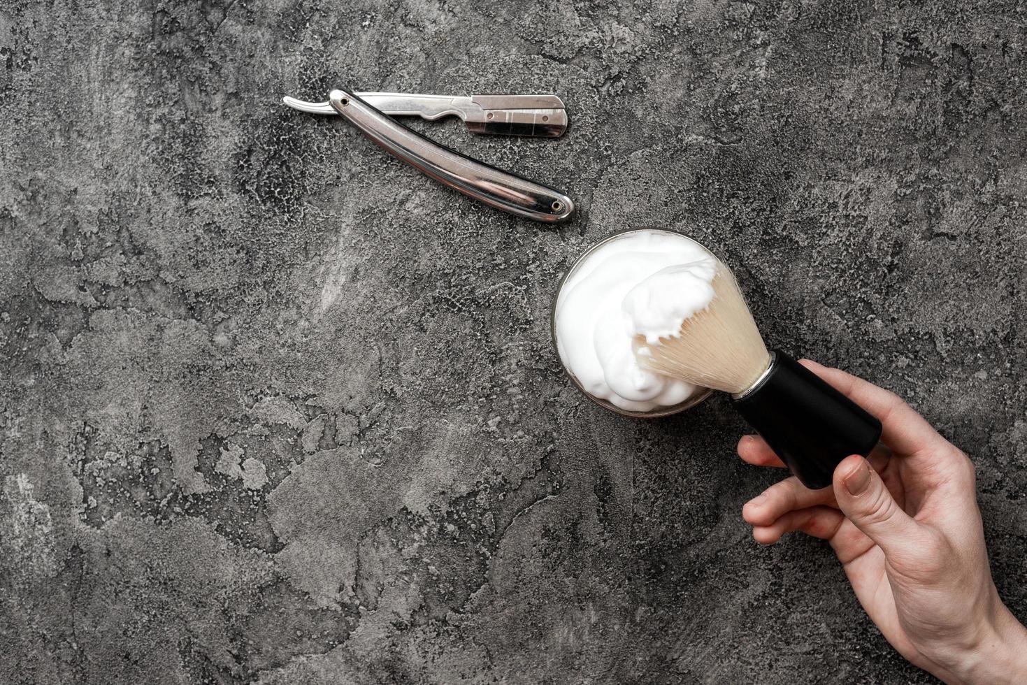 Shaving accessories on gray, plaster background. Tools. Disposable shaving razor, brush, cream. photo