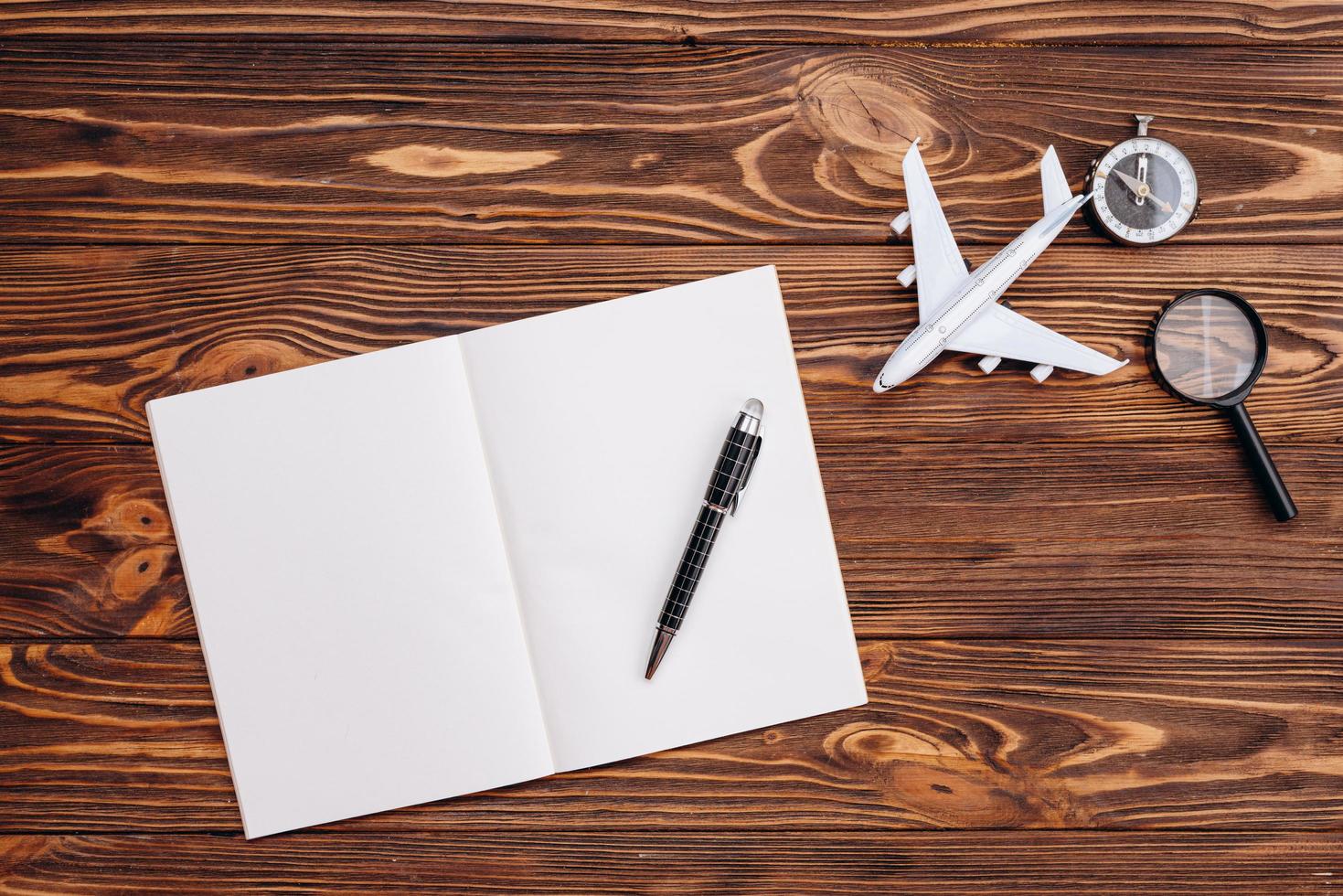 On a wooden surface a blank sheet of paper and a pen, an airplane and a compass, travel concept photo