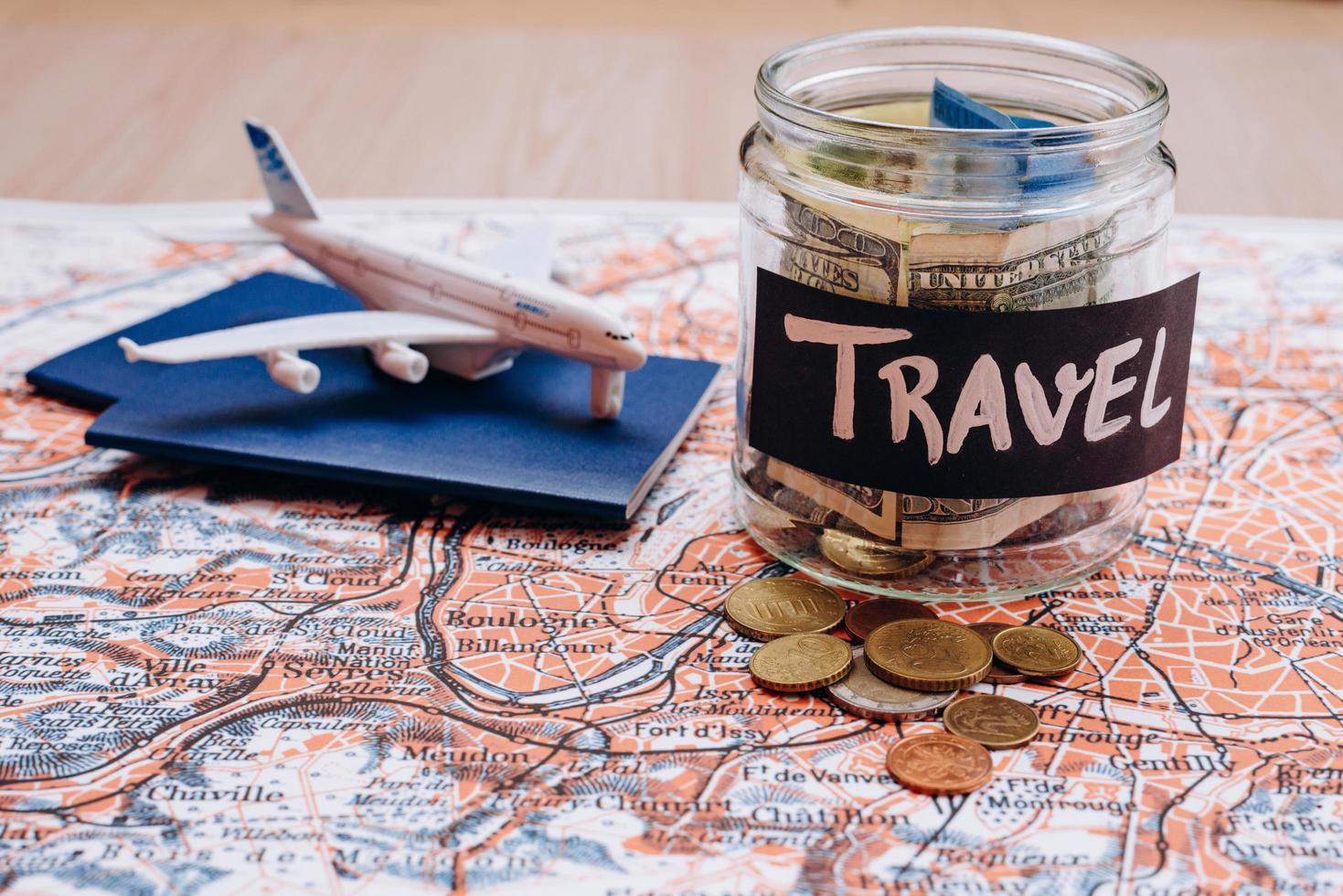 Vacation money savings in a glass jar with travel text . World map background photo