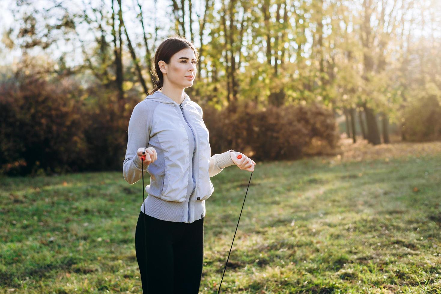 Pretty, slim girl jumping on skipping rope outdoors photo