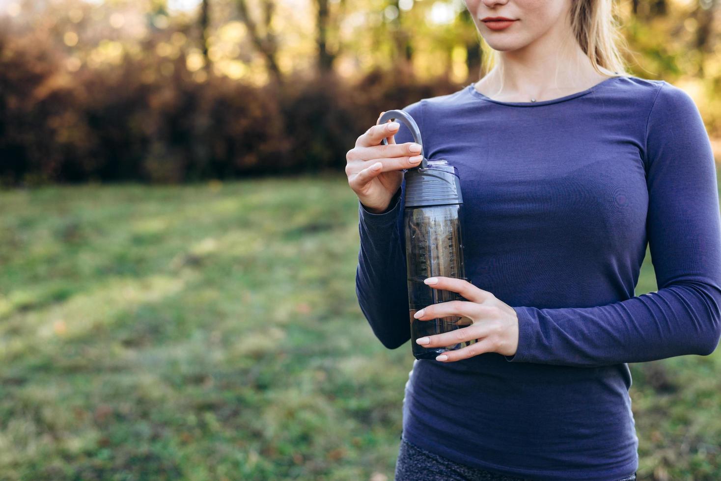 Young athletic woman opening a water bottle while workout outdoors, outdoors. Copy space. photo