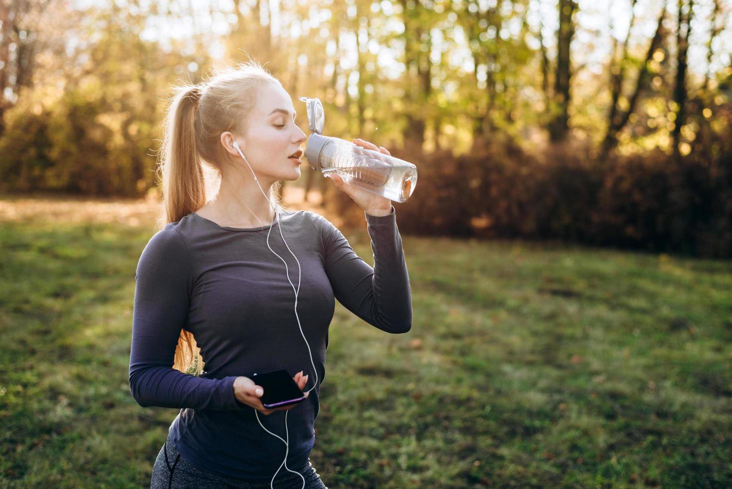 A young, pretty girl in headphones drinks water after a workout. photo