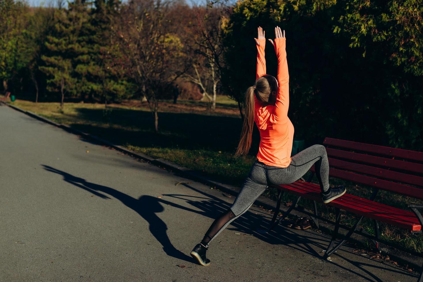 Chica joven fitness haciendo estiramientos mientras se apoya en un banco antes de correr al aire libre en el parque foto