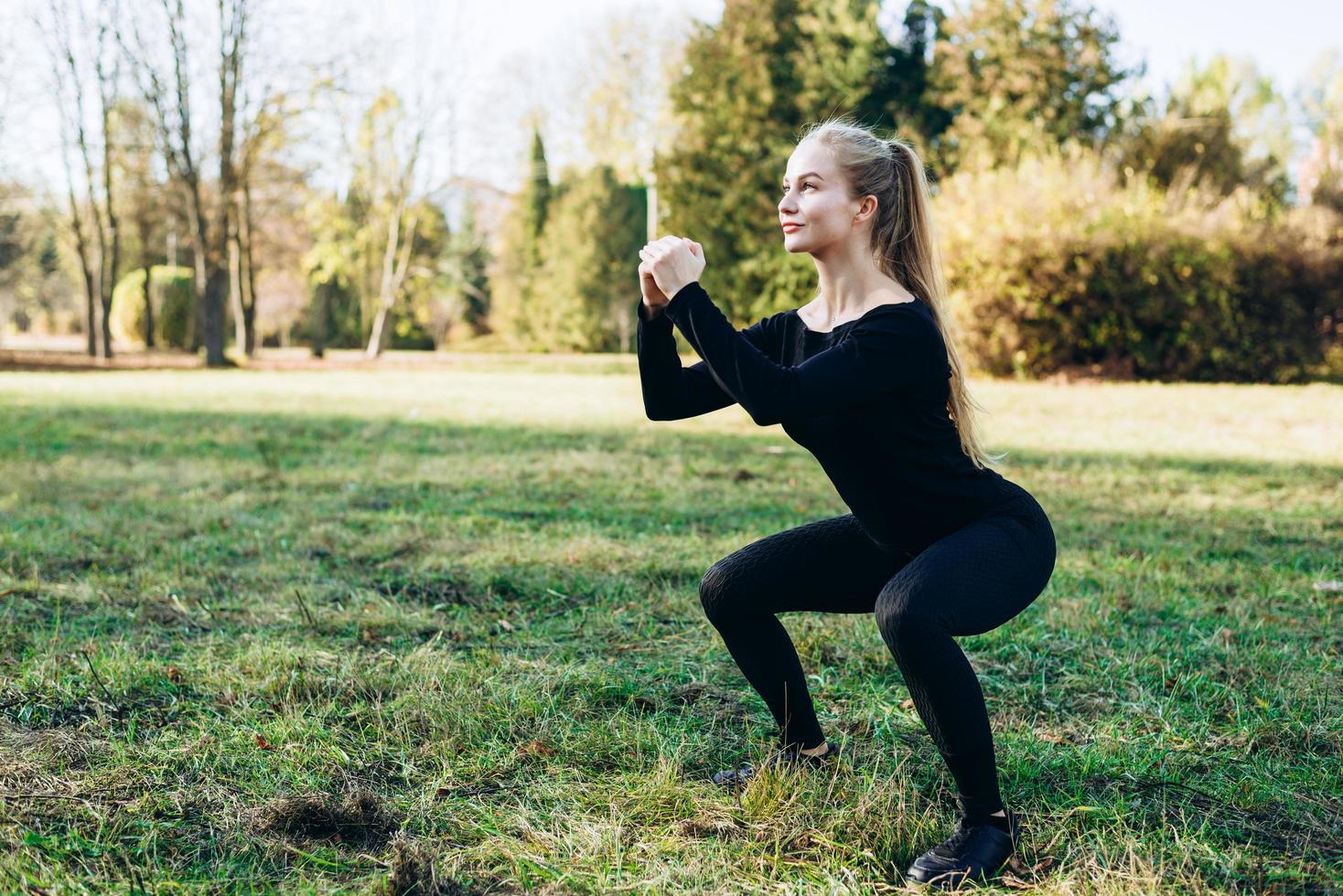 Pretty sporty girl doing squats during outdoor workouts photo