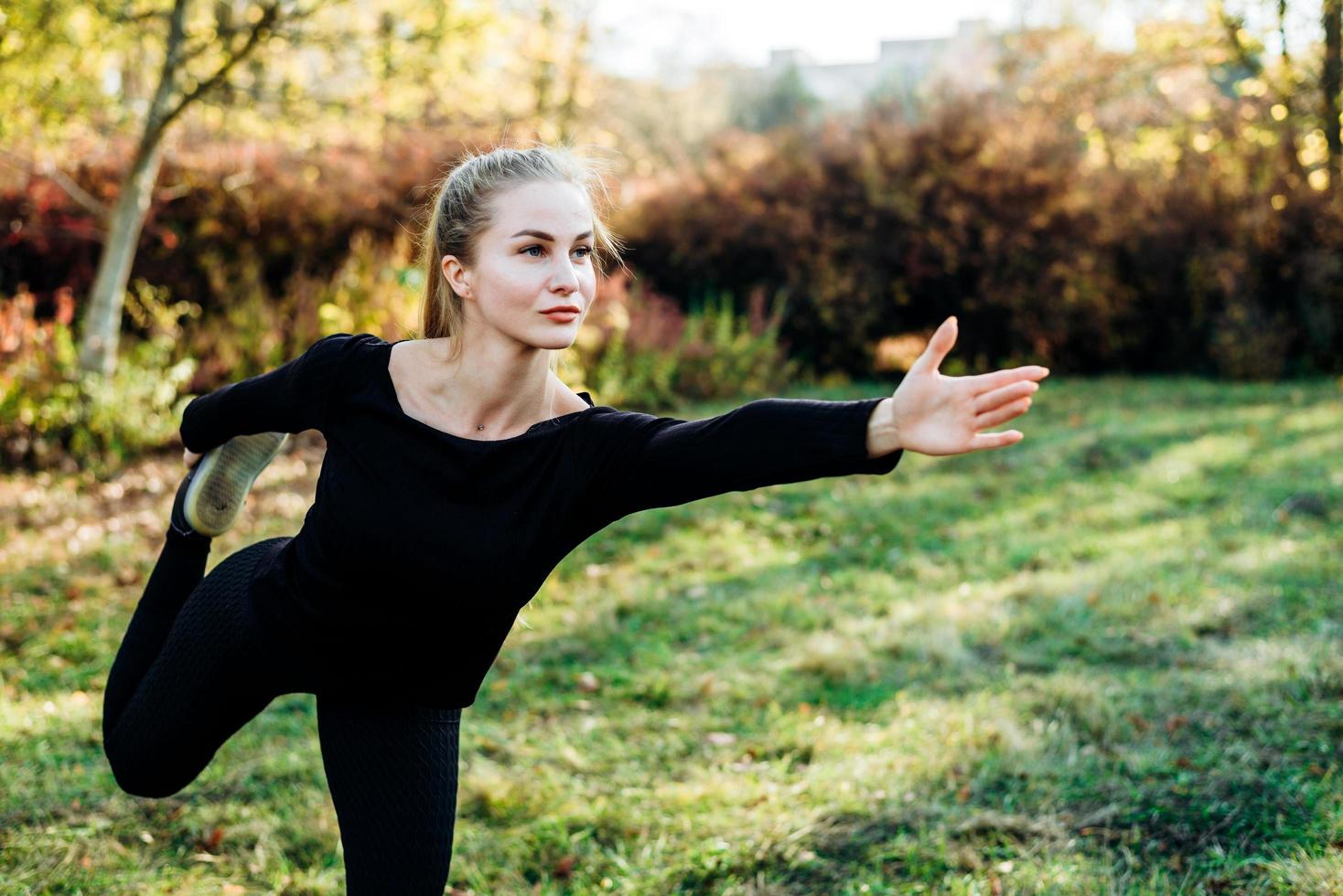 chica joven en ropa deportiva negra en una pose de equilibrio al aire libre. foto