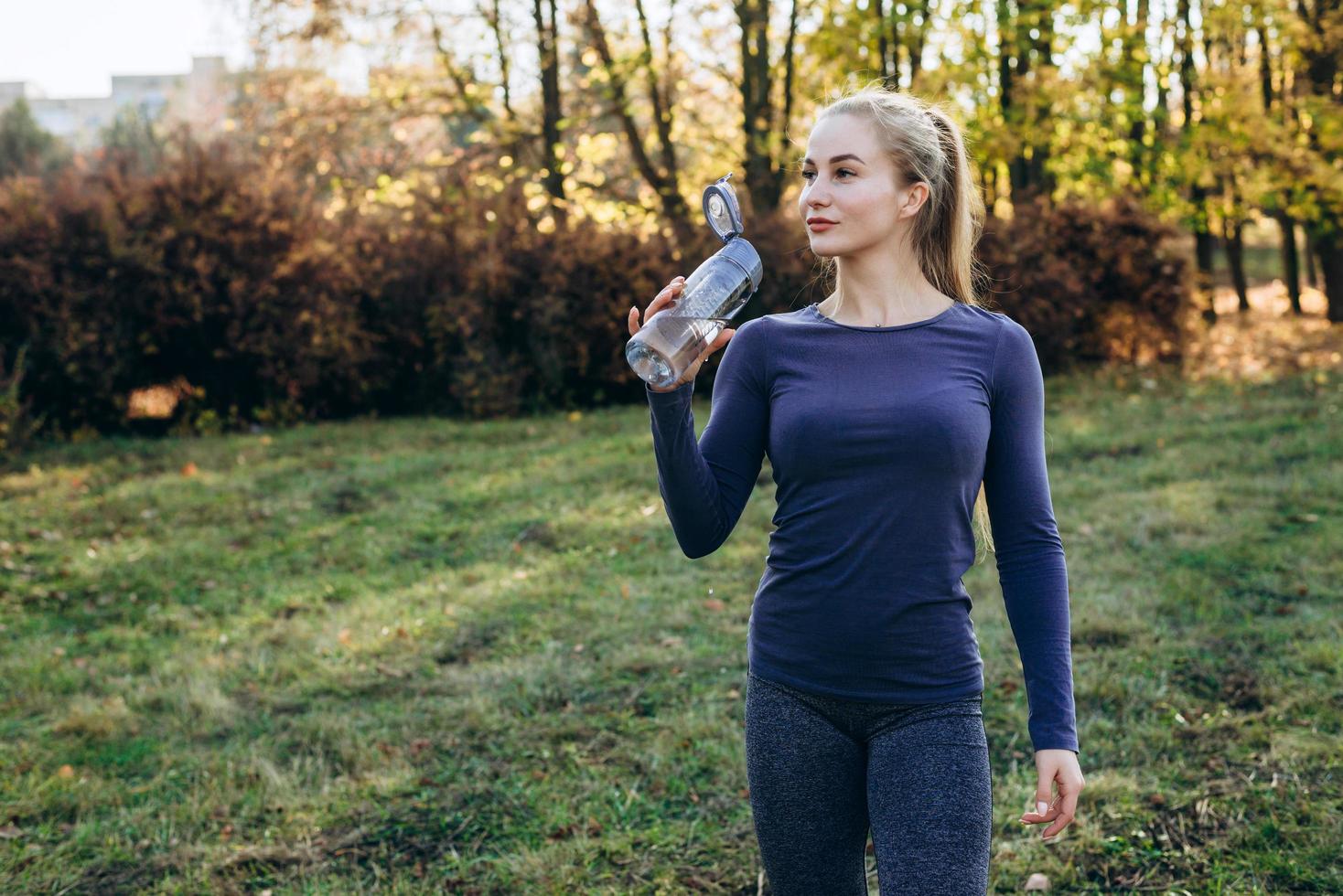 Fitness in the park, girl holds a bottle of water in her hand. photo