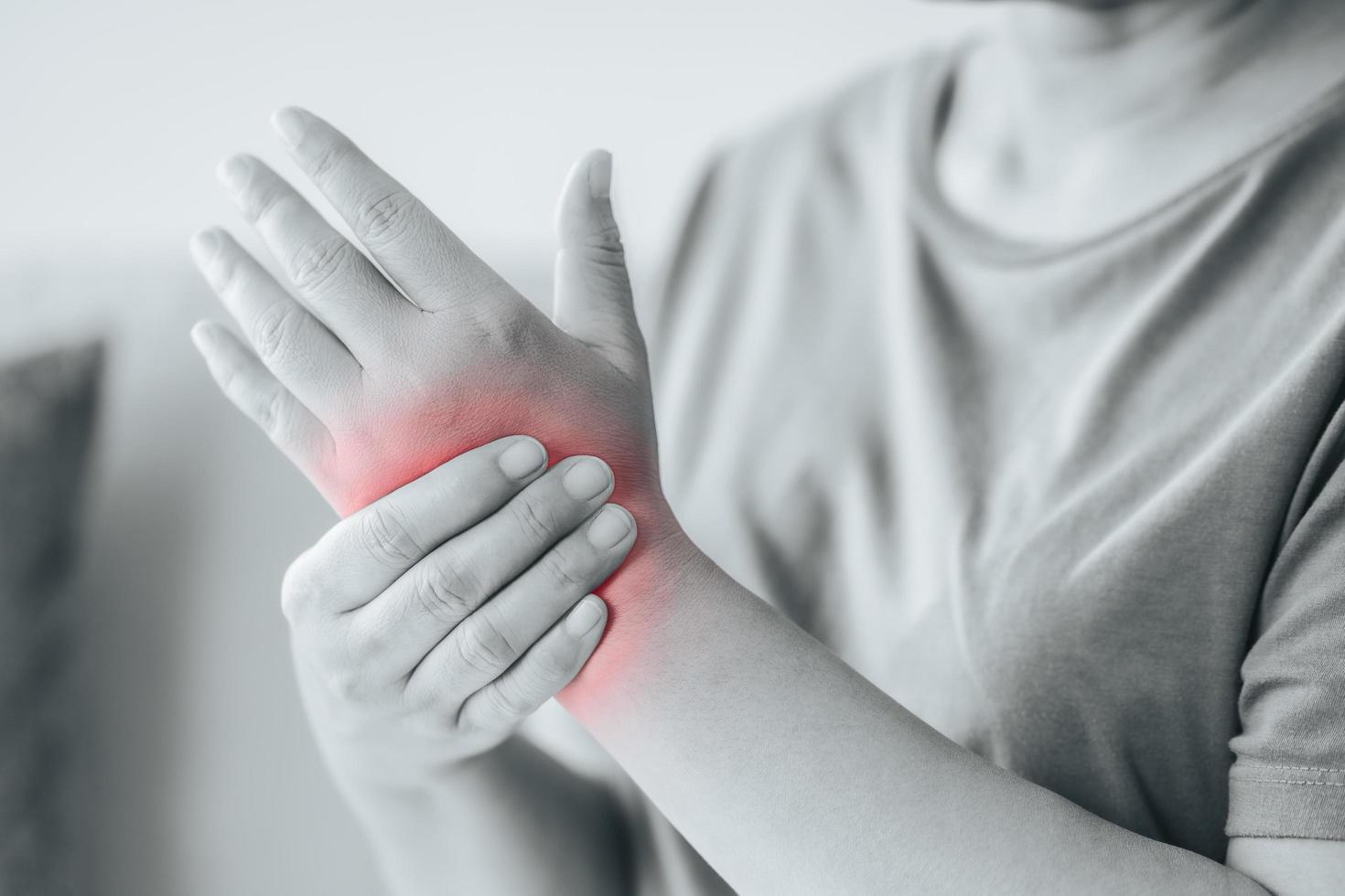 Closeup of woman sitting on sofa holds her wrist, hand injury with red highlight, feeling pain. Health care and medical concept. photo