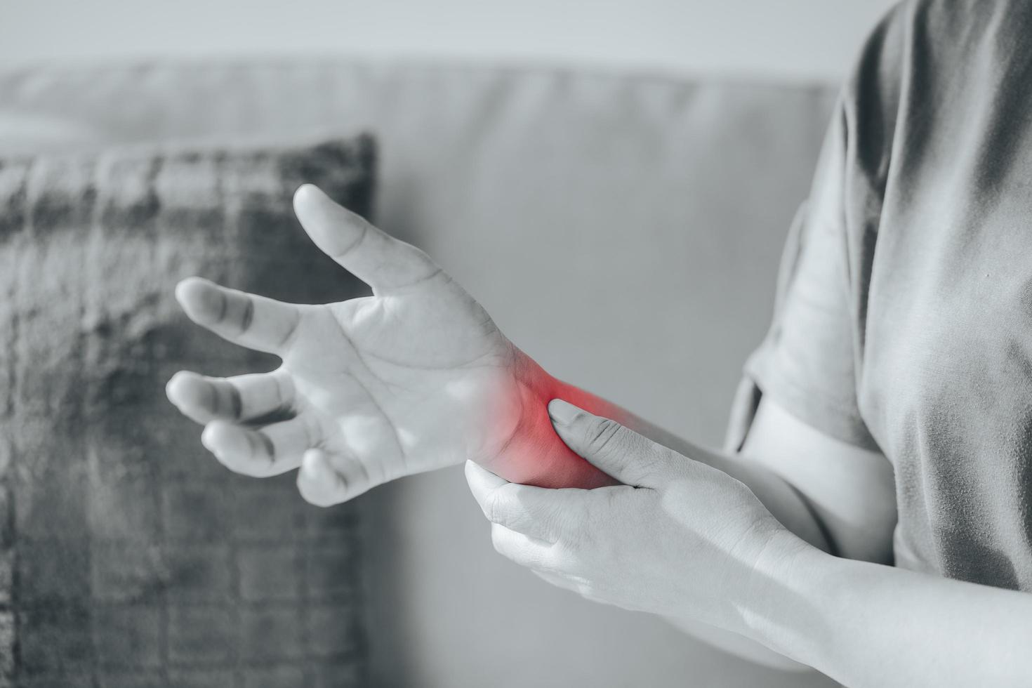 Closeup of woman sitting on sofa holds her wrist, hand injury with red highlight, feeling pain. Health care and medical concept. photo