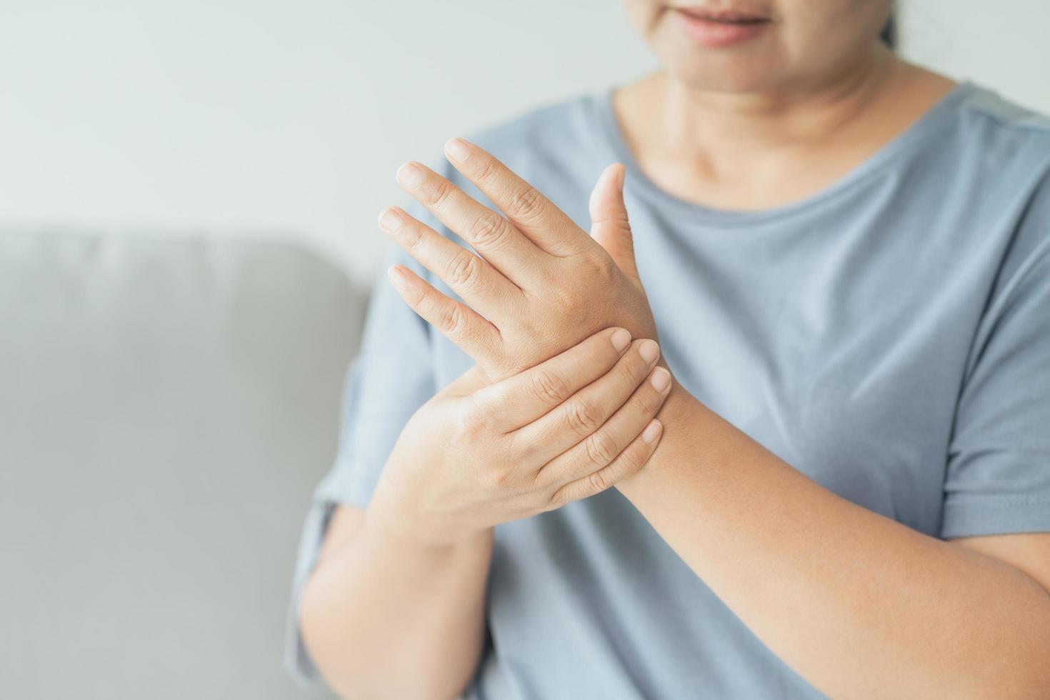 Primer plano de una mujer sentada en el sofá sostiene su muñeca. lesión en la mano, sensación de dolor. cuidado de la salud y concepto médico. foto