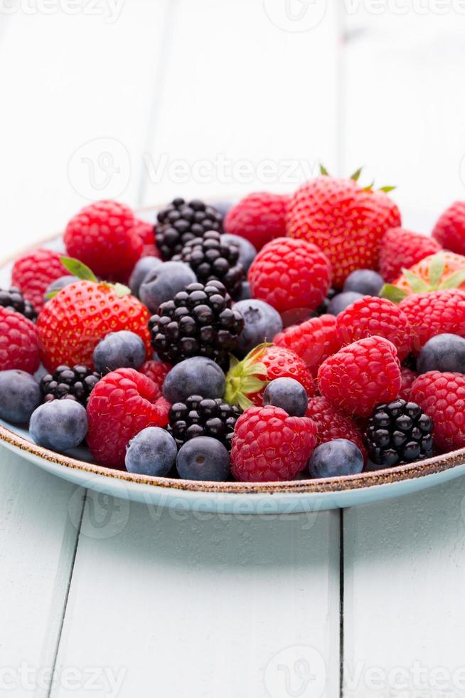 Fresh berry salad on blue dishes. Vintage wooden background. photo