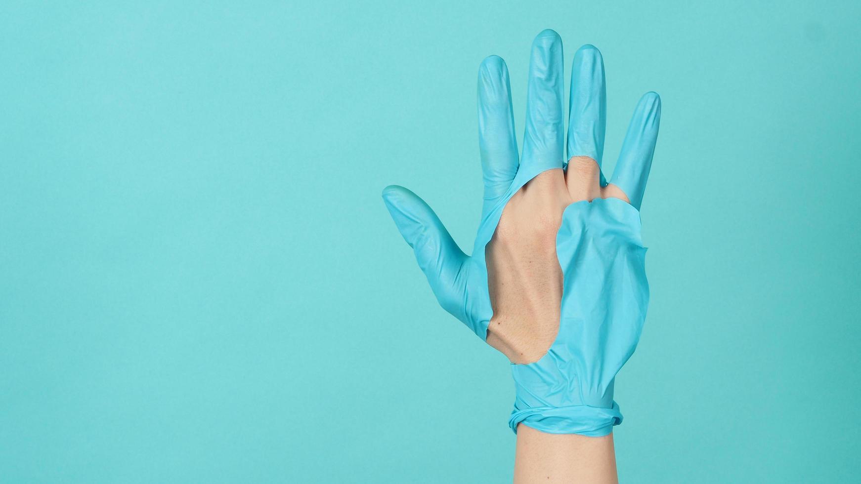 mano con guantes médicos rotos o guantes de goma rotos sobre fondo de color azul y verde o azul tiffany. coclor monótono. foto