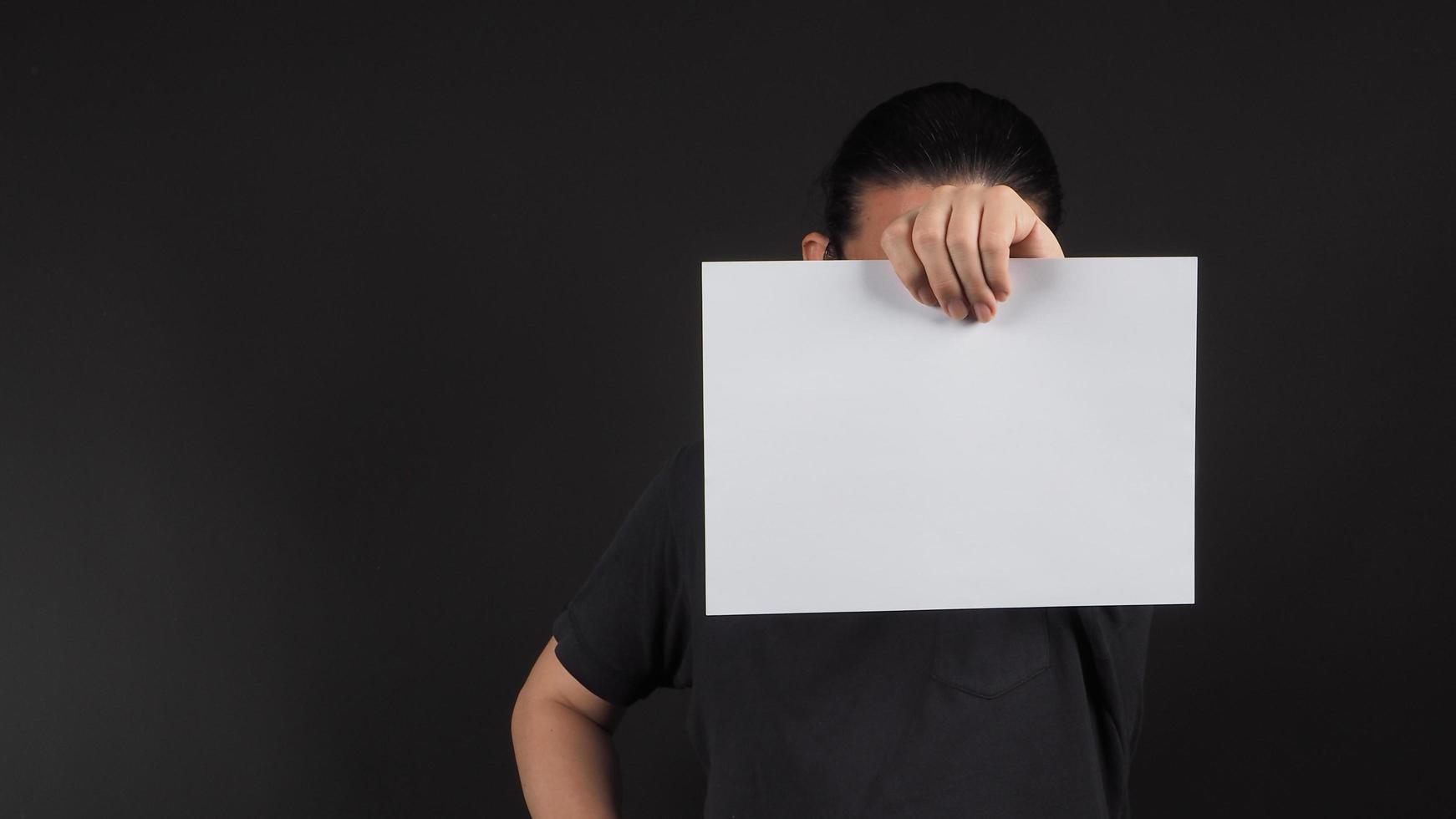 La mano izquierda del modelo masculino sostiene papel a4 en blanco sobre fondo negro. foto