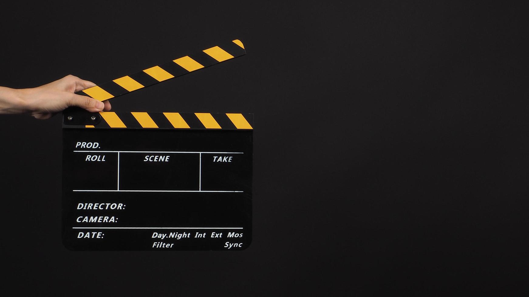 Hand is holding Black with yellow color clap board or movie slate use in video production and movie industry on black background. photo