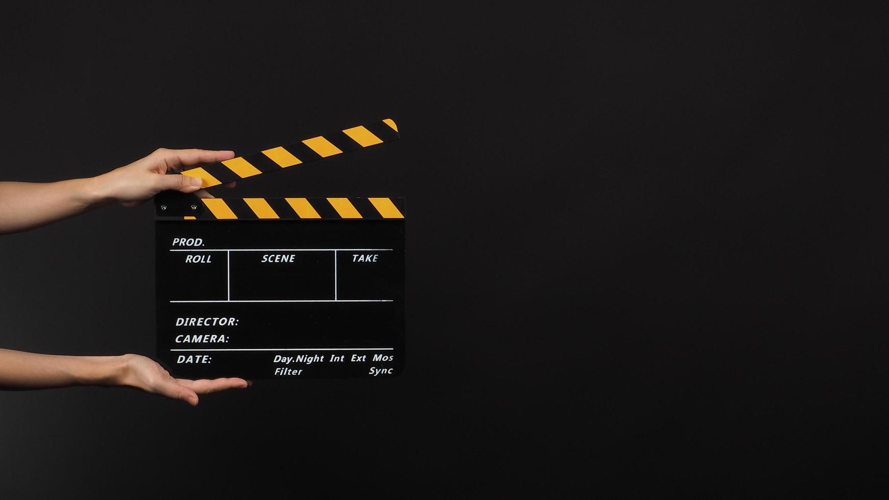 Hand is holding Black with yellow color clap board or movie slate use in video production and movie industry on black background. photo