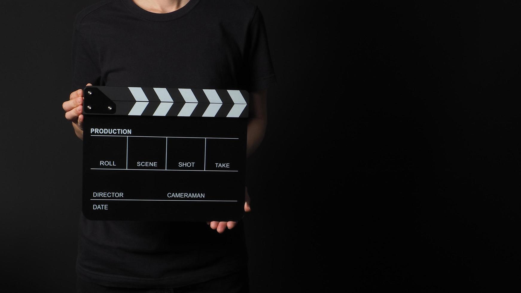 Female model is holding clapperboard or movie slate in studio shooting .It is use in video production and cinema industry on black background. photo