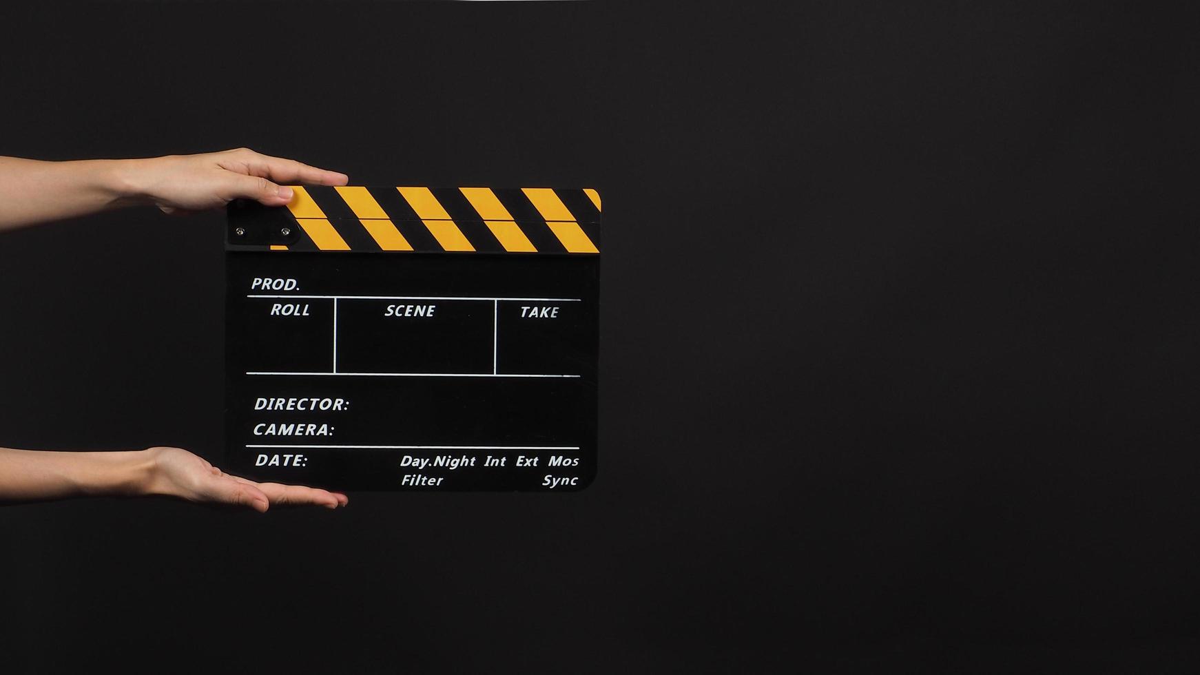 Hand is holding Black with yellow color clap board or movie slate use in video production and movie industry on black background. photo