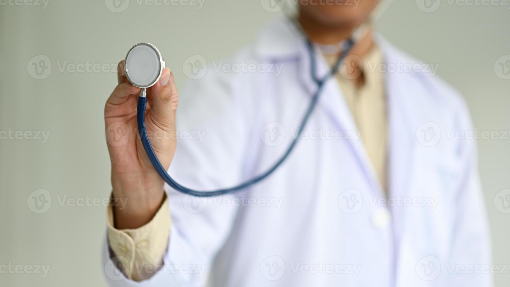 Toma recortada de un médico con una bata de laboratorio sostiene un estetoscopio al frente, conceptos médicos. foto