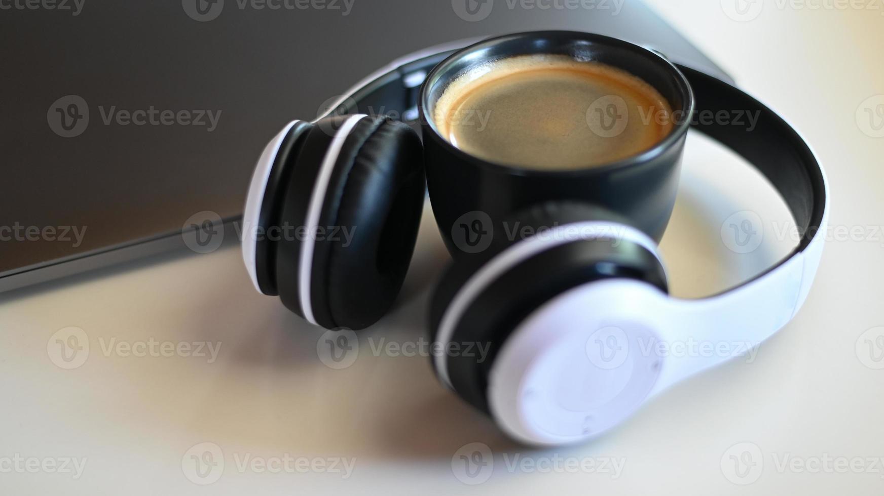 Taza de café con computadora portátil y auriculares colocados sobre una mesa en un café, lugar de la taza de café en los auriculares. foto