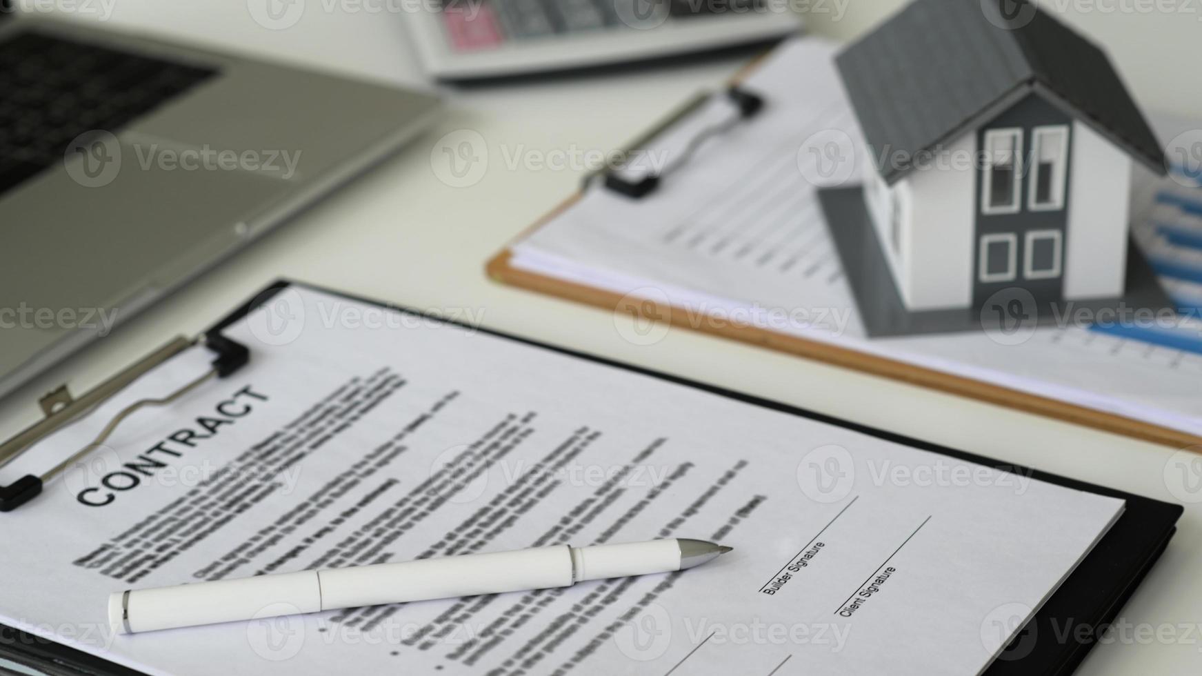 bolígrafo con documentos para firmar contrato de construcción de casa con modelo de casa y portátil, concepto de bienes raíces, primer plano. foto