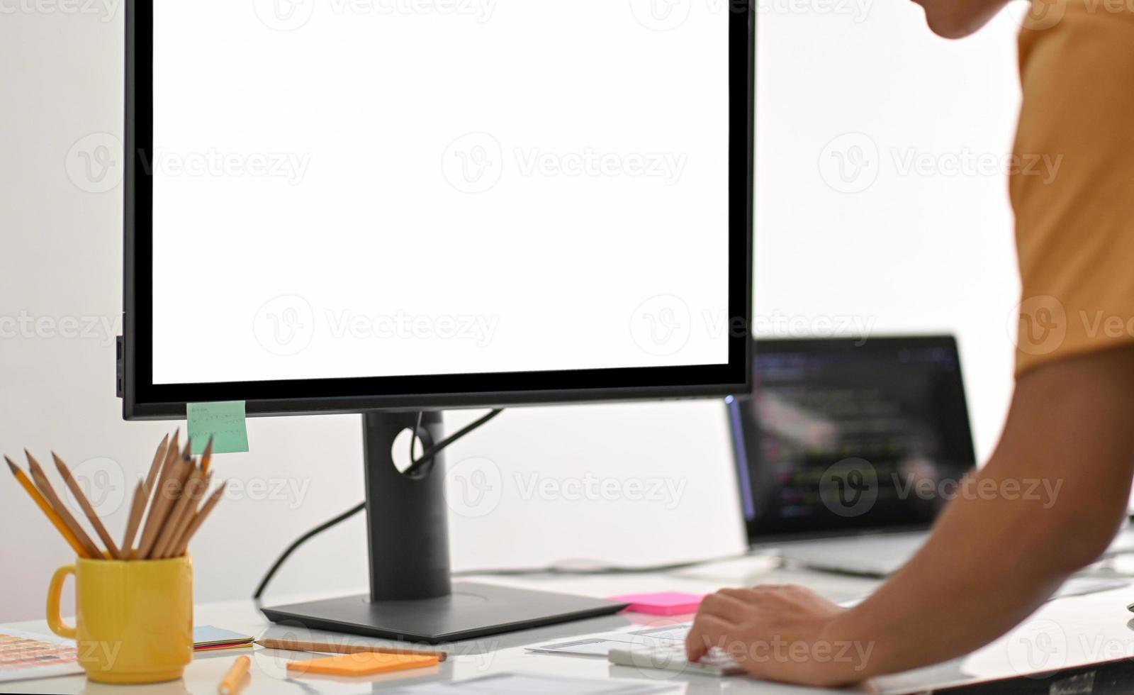 A young man standing and using a computer with a blank screen on a white table. photo