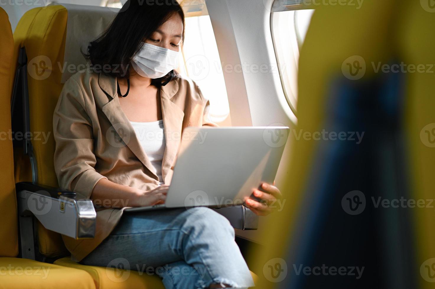 mujer con máscara está usando su computadora portátil durante un vuelo en avión. foto
