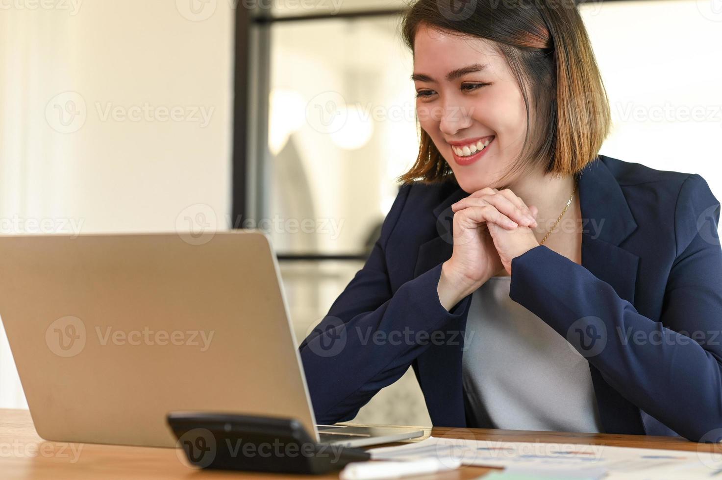 sonriente empresaria en un traje está teniendo una videoconferencia con su computadora portátil. foto