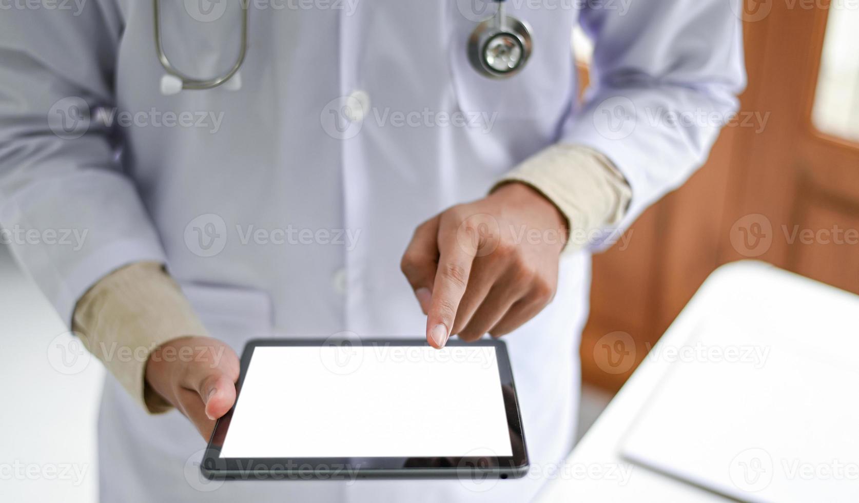 Man in medical gown standing, holding a blank screen tablet in front. photo