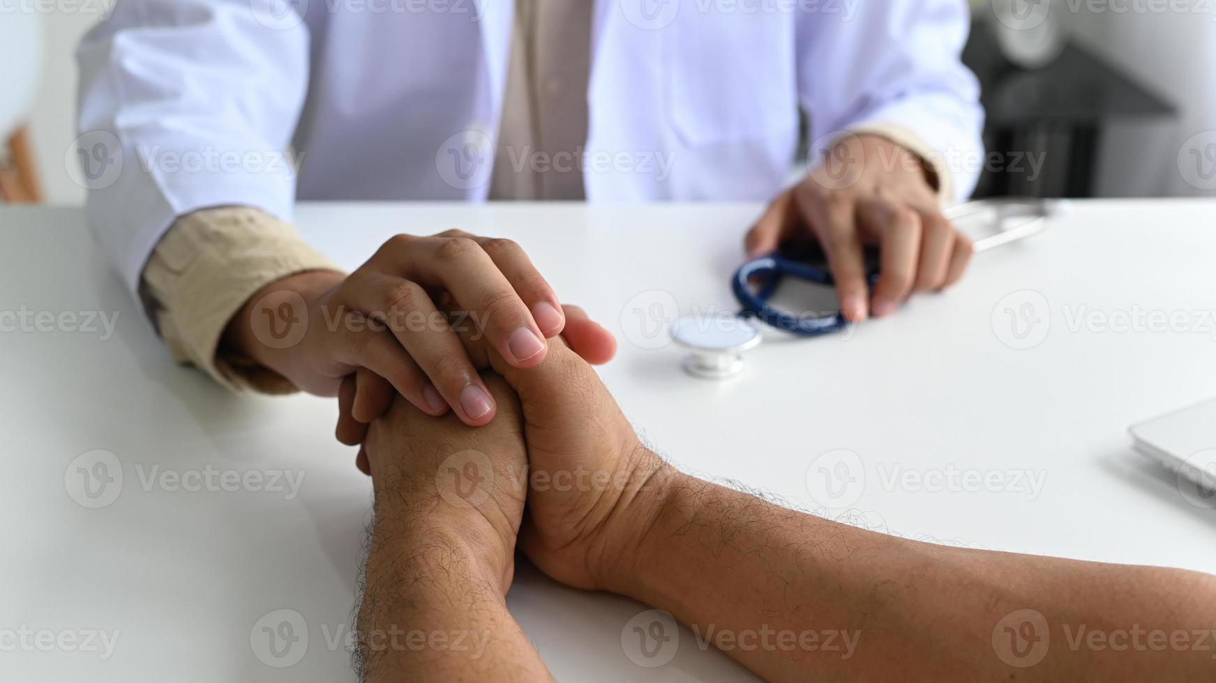 A medical professional in a lab gown with a stethoscope holds the patient hand to comfort, The doctor grabs the patient's hand to encourage. photo