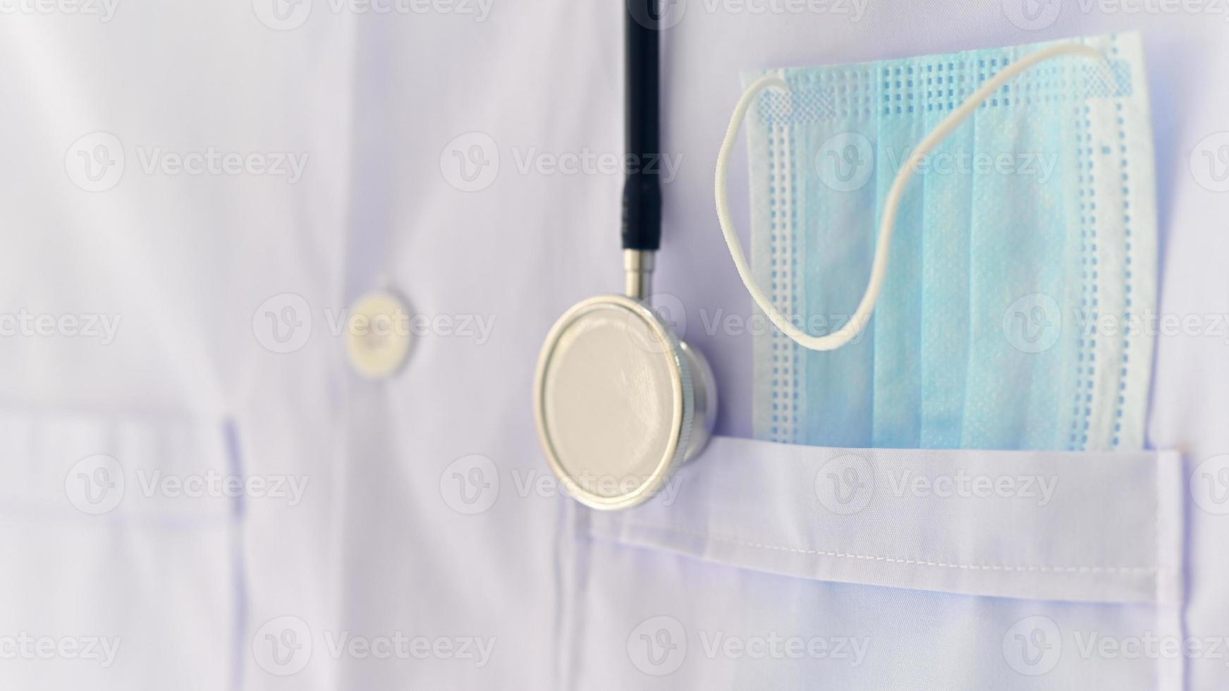 Primer plano de la máscara en la bata de laboratorio de bolsillo y un estetoscopio, conceptos médicos. foto
