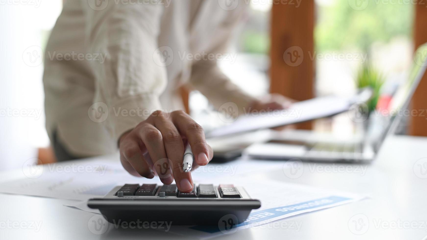 Primer plano de un joven sosteniendo un bolígrafo y usando una calculadora colocada en el frente.Conceptos de negocio. foto