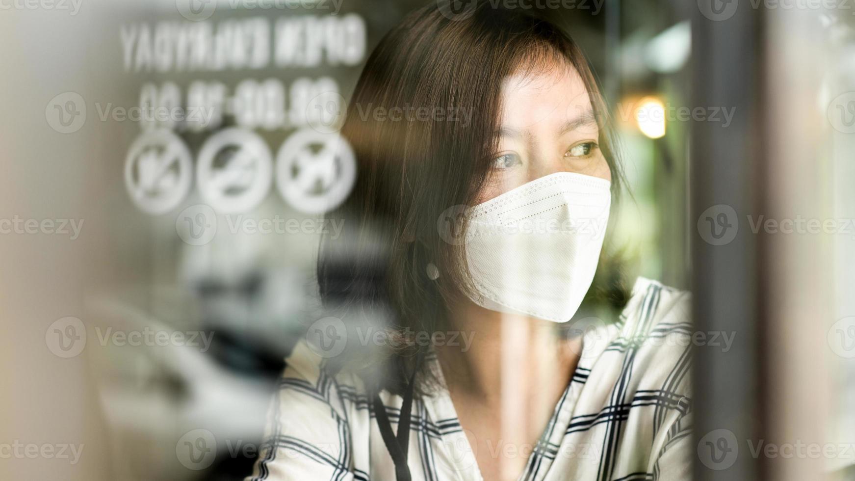 Mujer asiática con una máscara médica mirando por la ventana de un café. foto