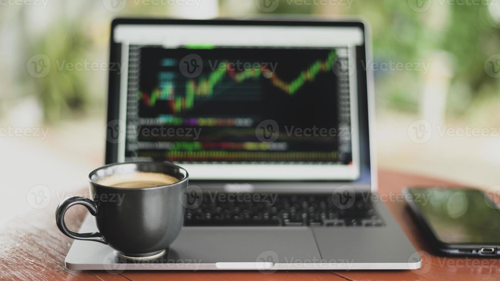 Coffee mug placed on laptop with stock graph on screen. photo