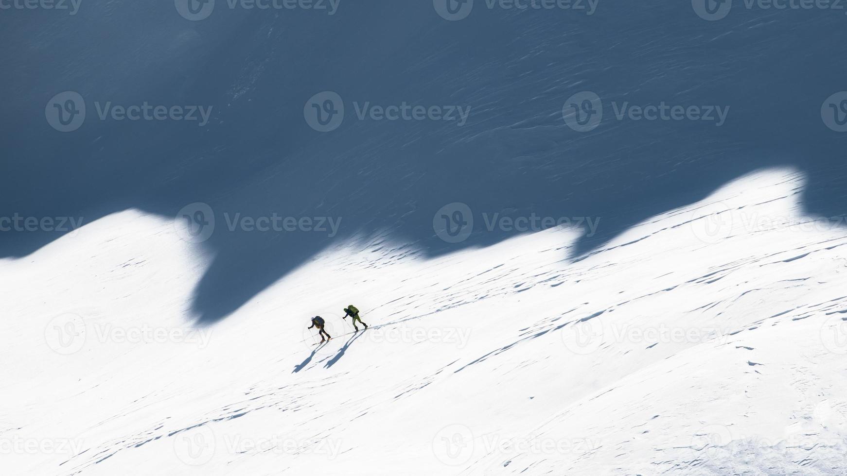 Ski mountaineers in the shadows of the mountains photo