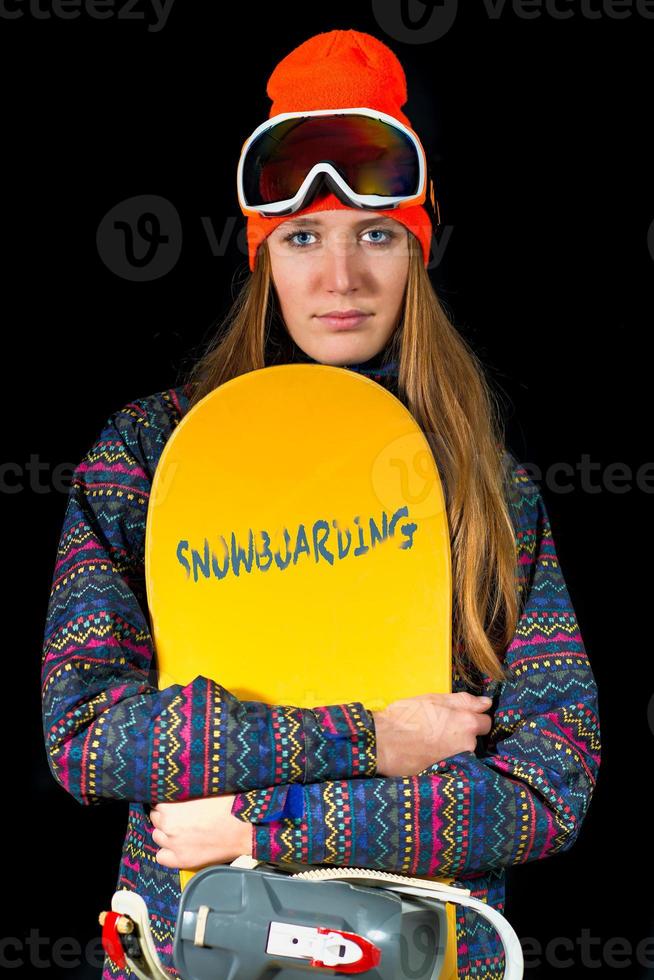 Chica rubia con pelo largo con snowboard y ropa deportiva de invierno y pasamontañas en studio foto